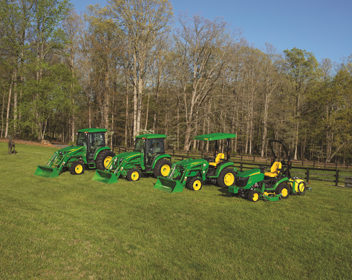 Four John Deere compact utility tractors are parked in a line in a field of grass on a sunny day 
