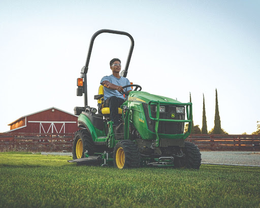 Man riding John Deere Tractor in front of a barn.