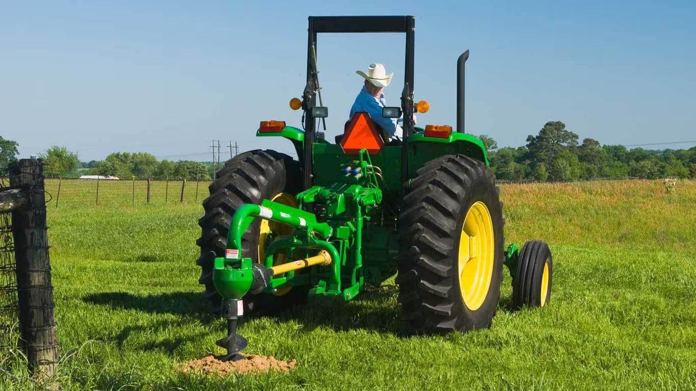 John Deere compact utility tractor with post hole digger attachment.
