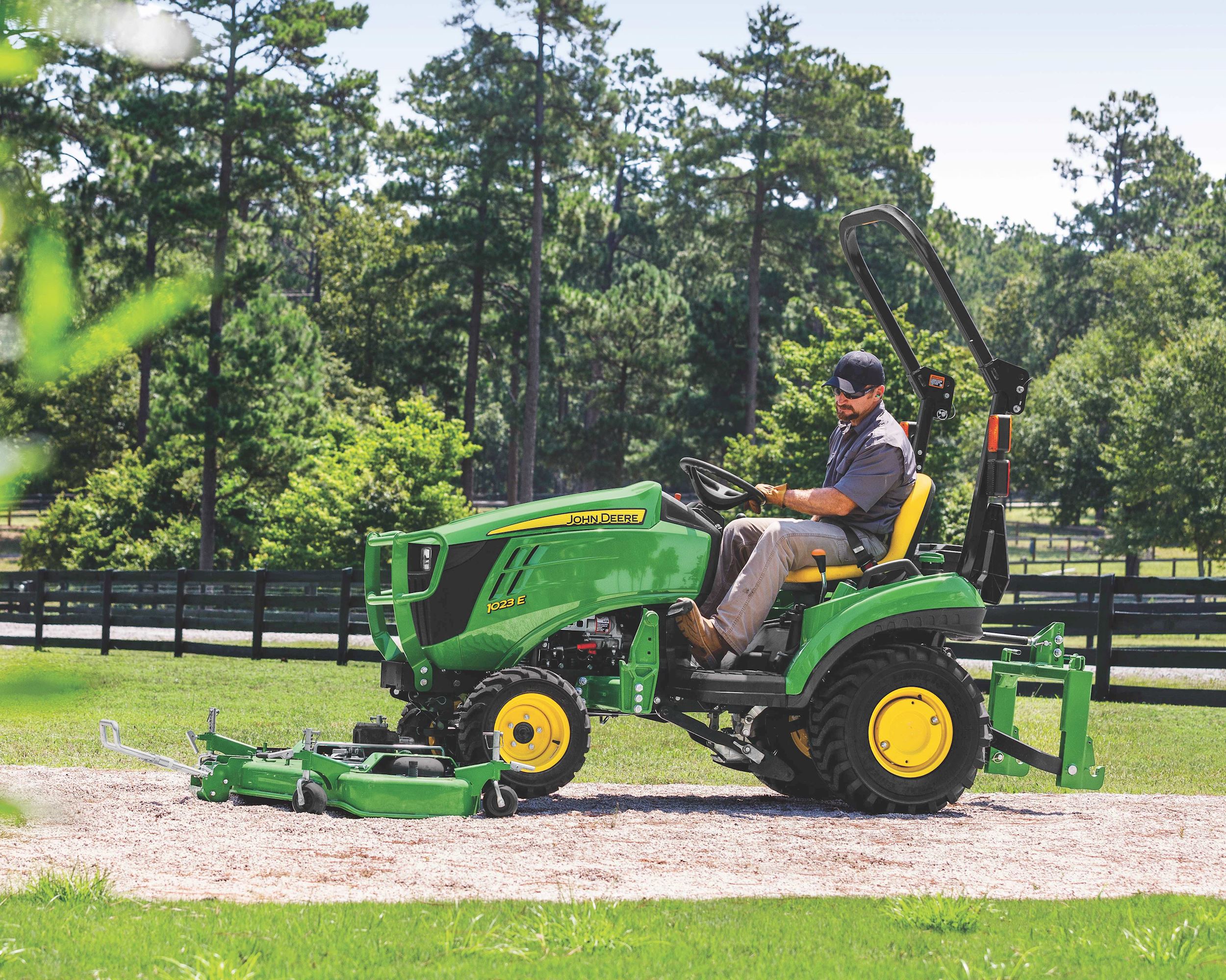 A man uses a John Deere 1023E tractor to cut grass.