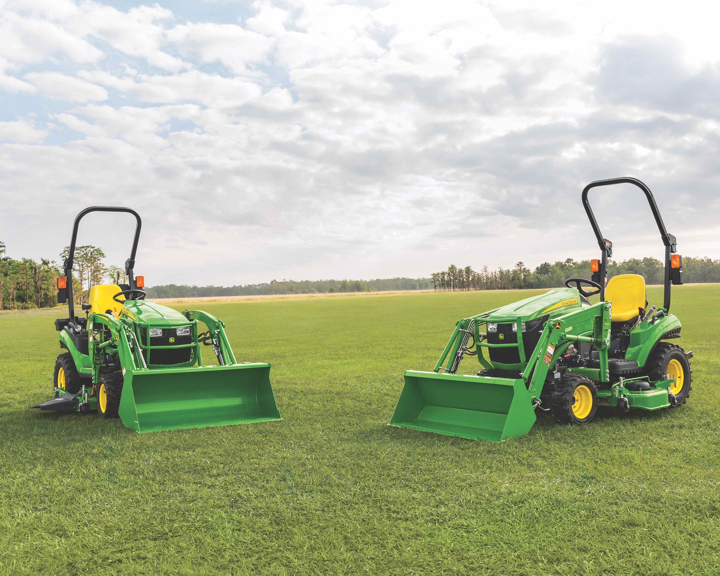 John Deere 1023E and 1025R tractors are parked on a field of grass with a blue sky in the background