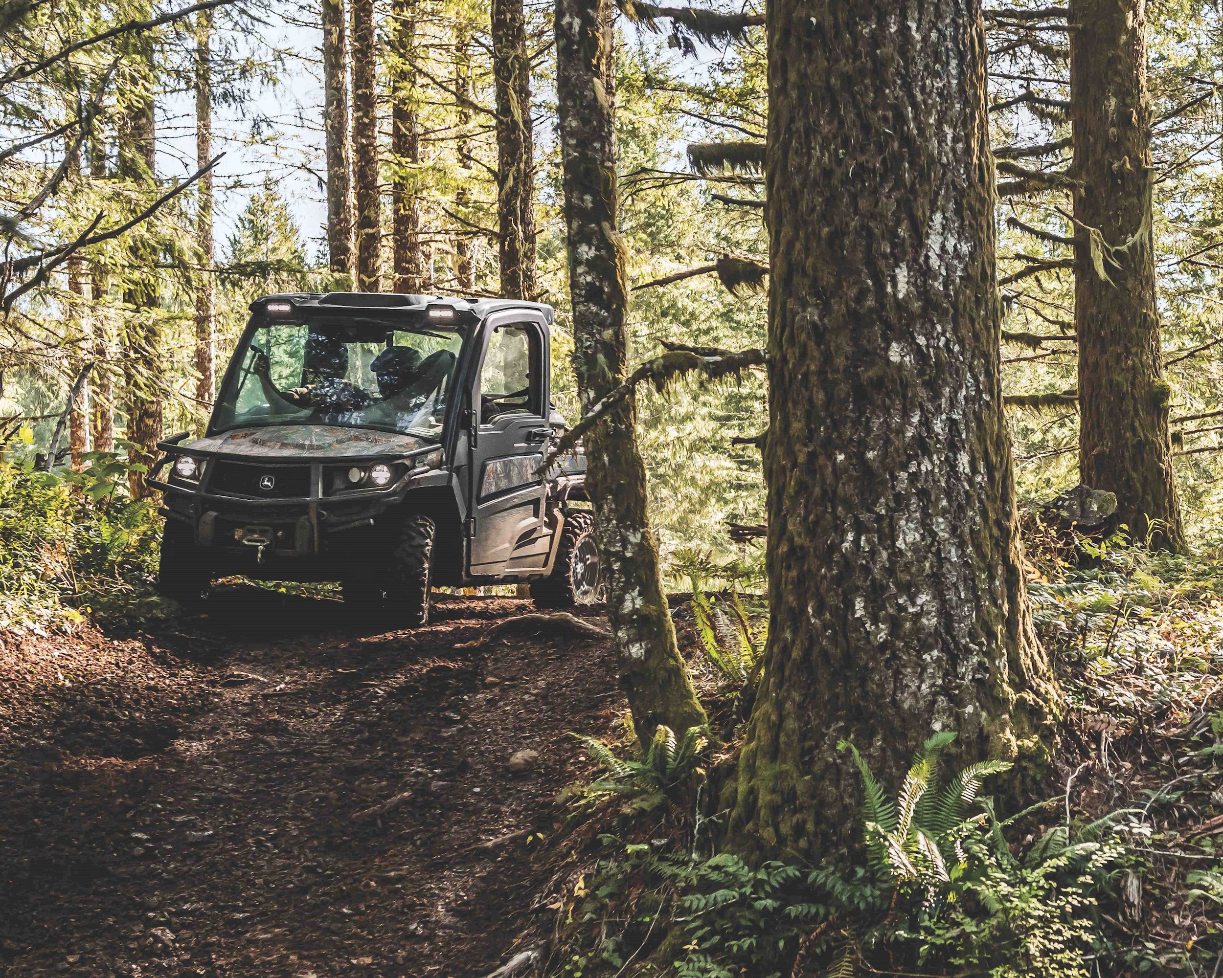 A camo John Deere Gator Utility Vehicle drives through the woods.