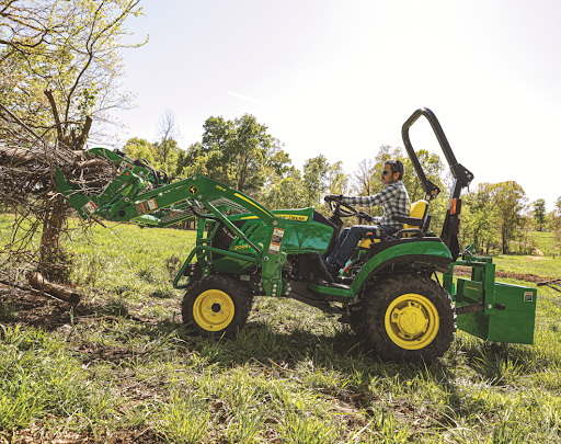 A man uses a tractor with grapple attachment to move brush 