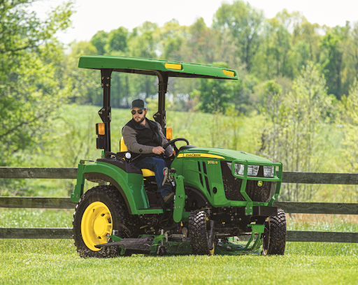 A man uses a 2 Series John Deere tractor with mower deck to mow the grass 
