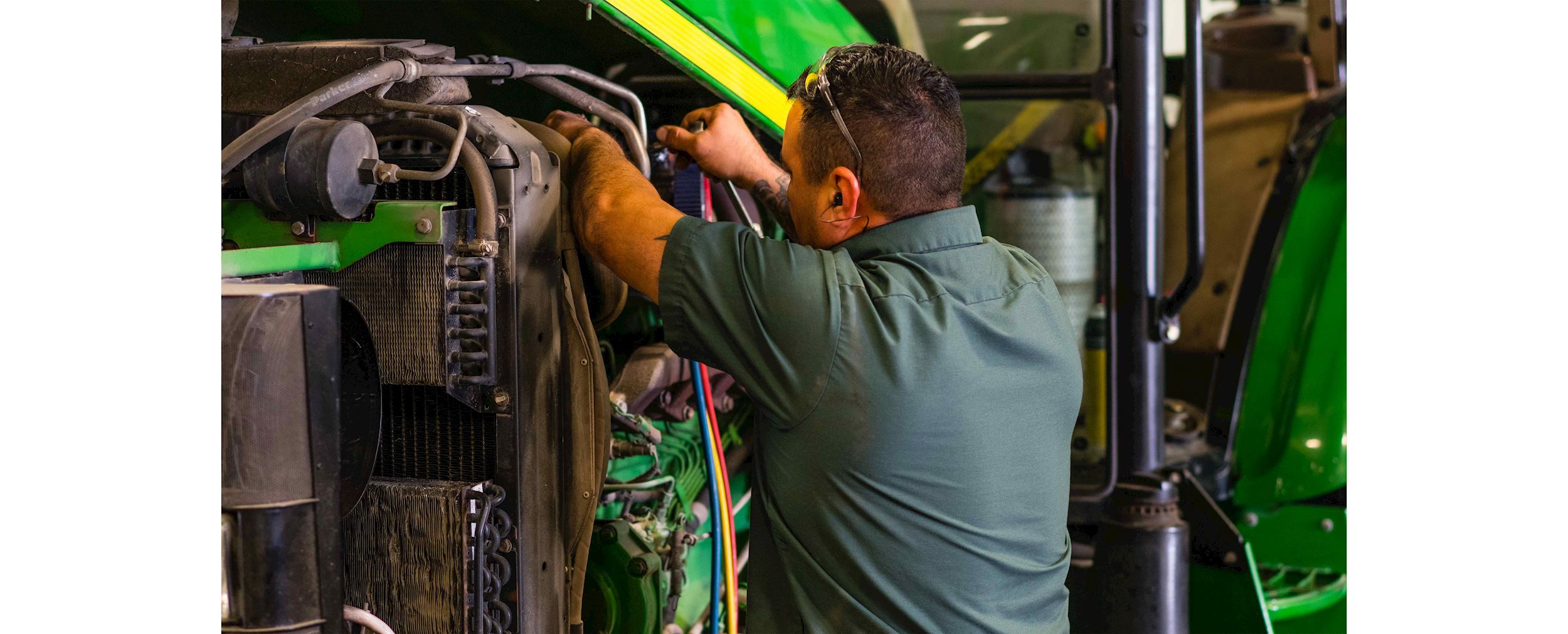 An Ag-Pro service technician works on a large piece of John Deere equipment in a garage.